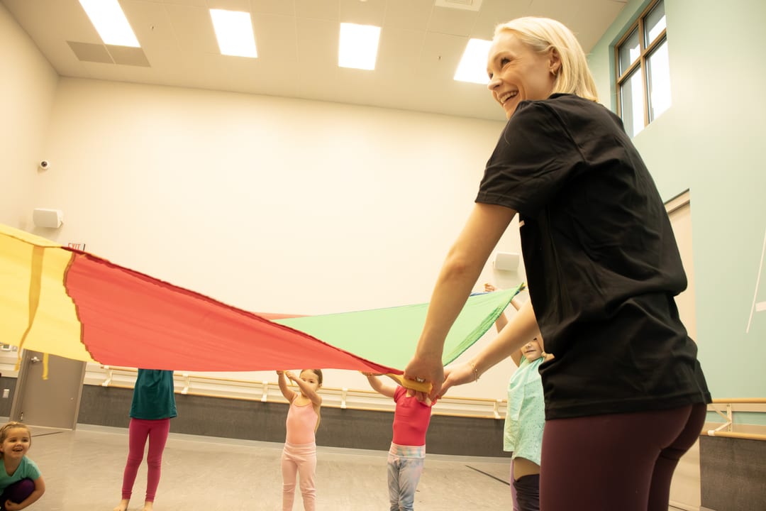 Children playing with a colorful parachute during summer dance camp